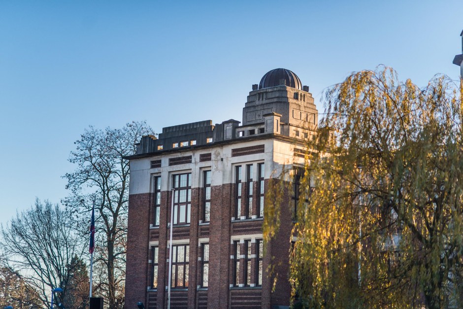 A brick-and-stone historic building with a domed tower framed by autumn trees and blue sky.